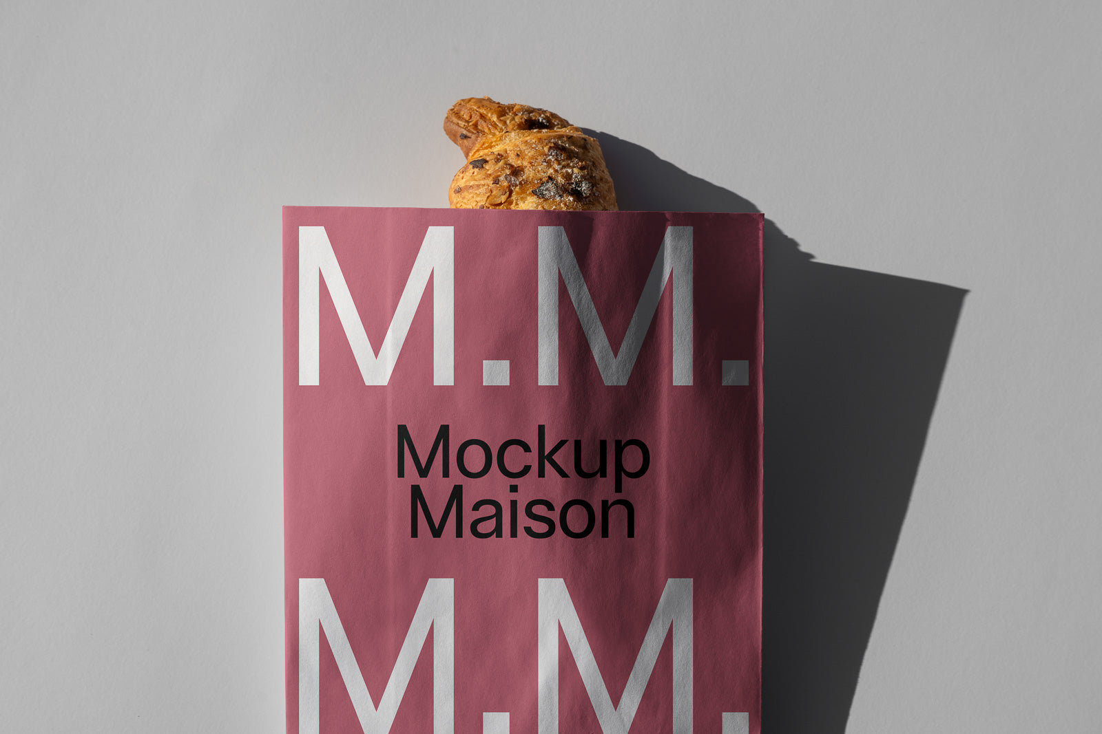 PSD mockup of a pink paper bag with "Mockup Maison" and "M.M." printed, partially filled with a croissant peeking out at the top.
