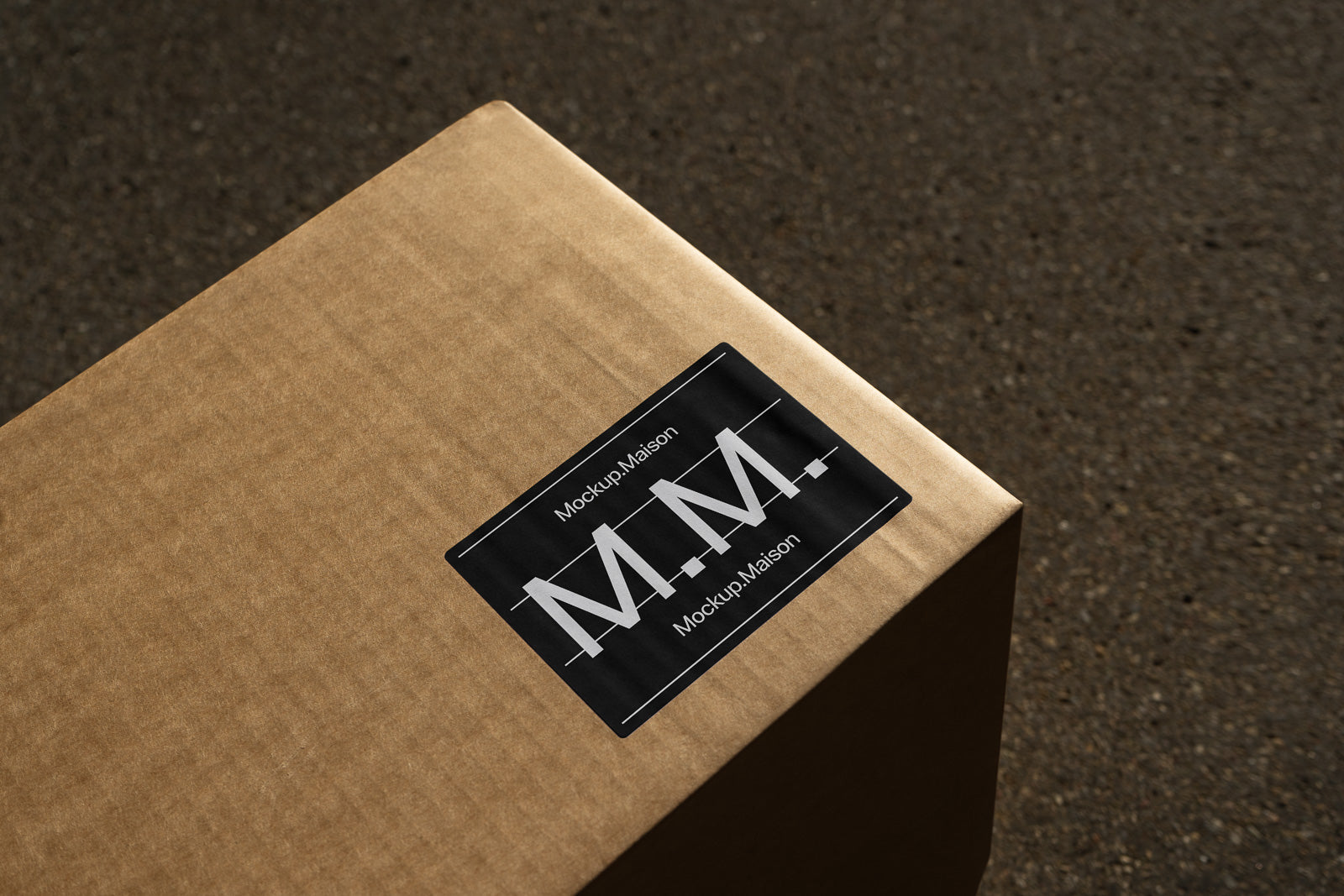 PSD mockup of a cardboard package with a dark label displaying "Mockup Maison" and the initials "M.M." on a textured surface.