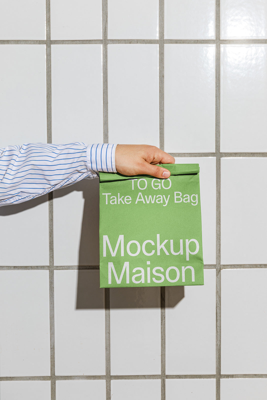 PSD mockup of a hand holding a green takeaway bag with white text against a tiled wall background.