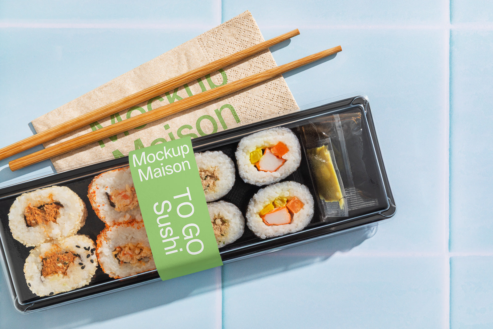 PSD mockup of a sushi to-go box containing assorted rolls with soy sauce and a wasabi packet, paired with wooden chopsticks on a blue surface.