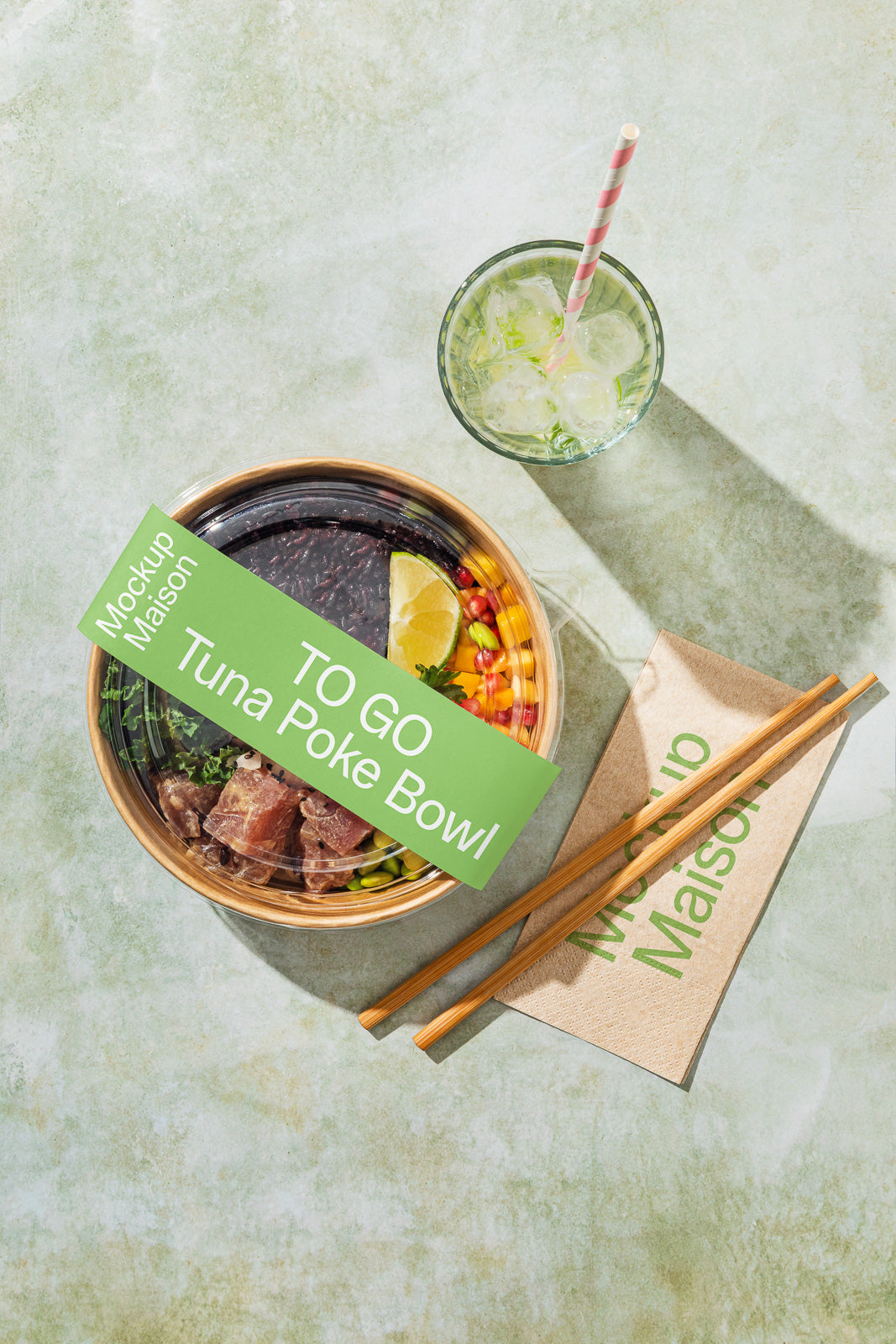 PSD mockup of a labeled poke bowl with tuna and various toppings, accompanied by a glass with a striped straw and chopsticks on a textured surface.