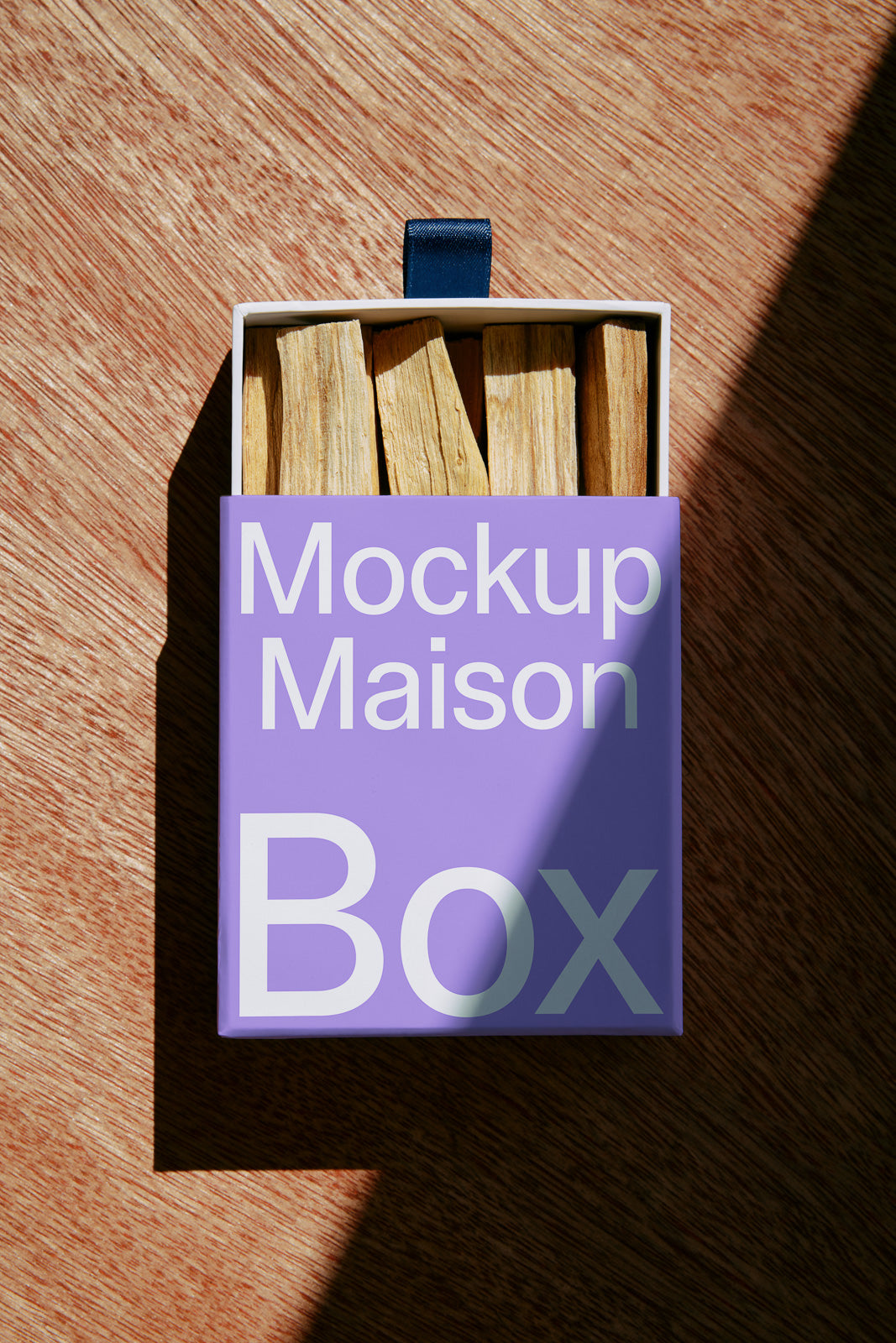 PSD mockup of an open box with wooden sticks inside, featuring "Mockup Maison Box" text on a purple lid, set against a wooden background.