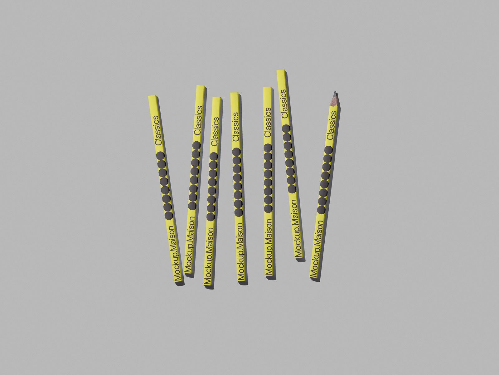 PSD mockup of seven yellow pencils with black dots and text, arranged in a slightly uneven line on a gray background.