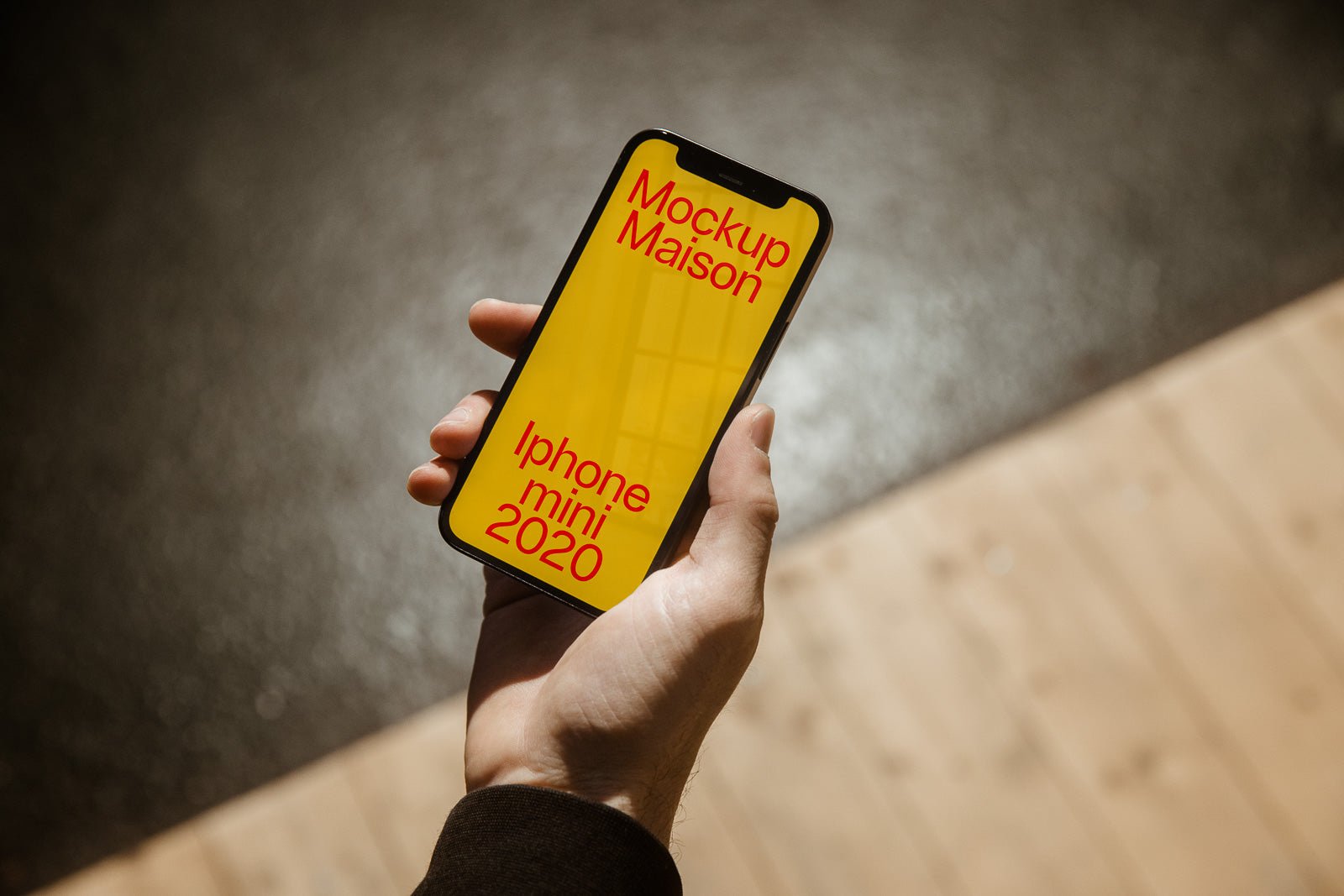 PSD mockup of a hand holding an iPhone with a yellow screen displaying text "Mockup Maison iPhone mini 2020," on a blurred background.