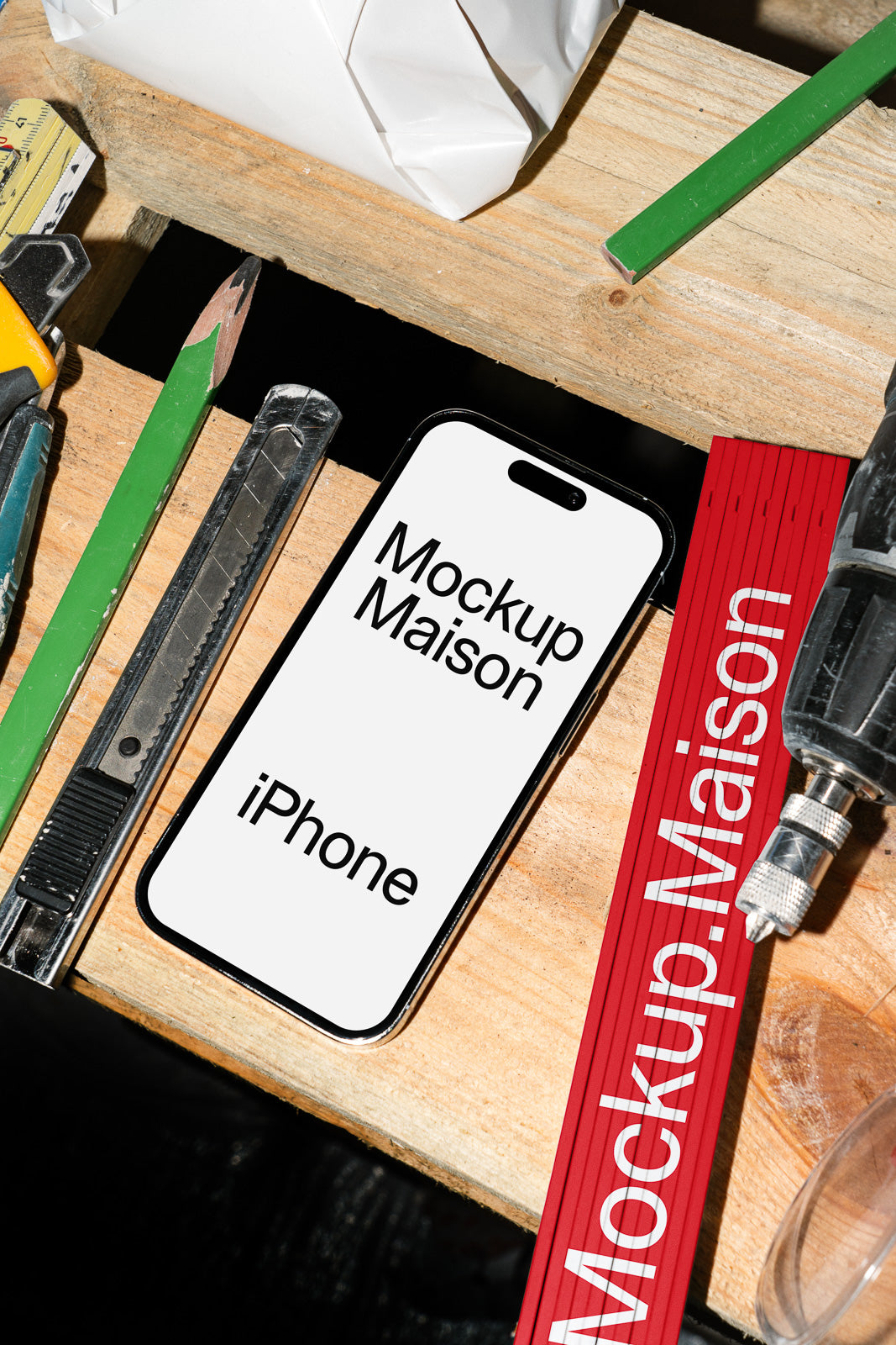 PSD mockup of an iPhone on a wooden desk surrounded by tools, including a ruler, pencil, utility knife, and drill.