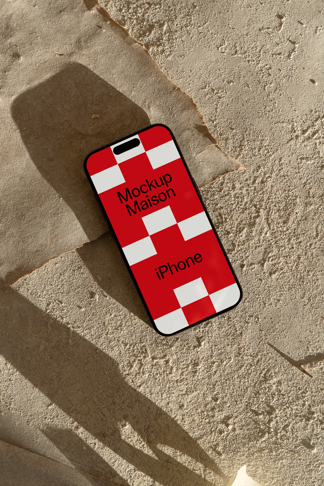 PSD mockup of an iPhone with a red and white checkered design, set on a sandy textured surface casting shadows.