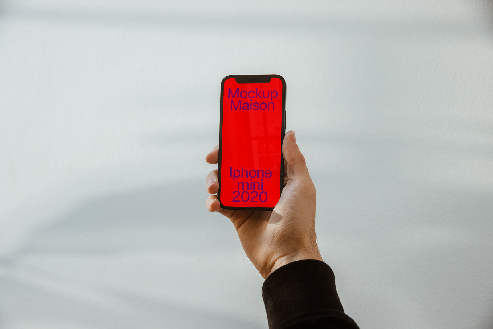 PSD mockup of a hand holding an iPhone with a red screen displaying text "Mockup Maison iPhone mini 2020" against a light background.