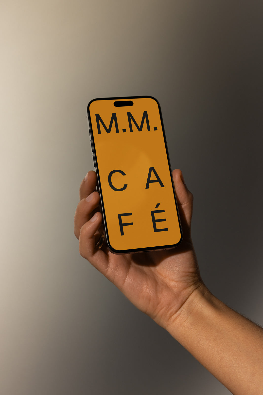 PSD mockup of a hand holding a smartphone displaying an orange screen with the text "M.M. CAFÉ" in bold black letters.