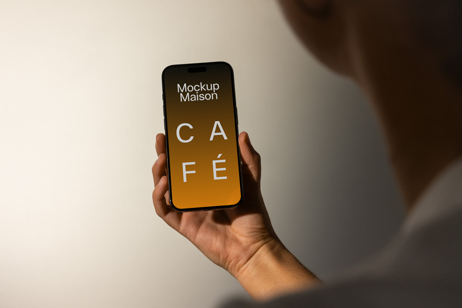 PSD mockup of a smartphone held in a hand with a screen displaying the words "Mockup Maison CAFÉ" on a gradient background.