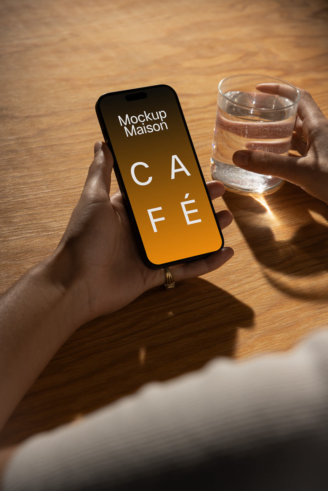 PSD mockup of a hand holding a smartphone displaying the word "Café" with another hand holding a glass of water on a wooden table.