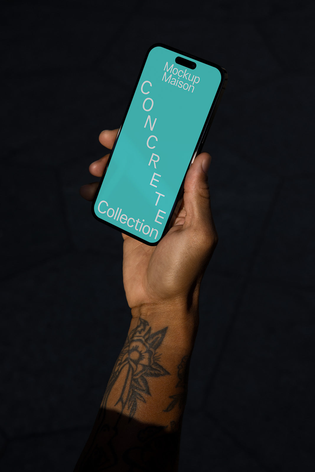 PSD mockup of a hand holding a smartphone displaying "Mockup Maison Concrete Collection" on a teal screen, with a tattoo visible on the forearm.