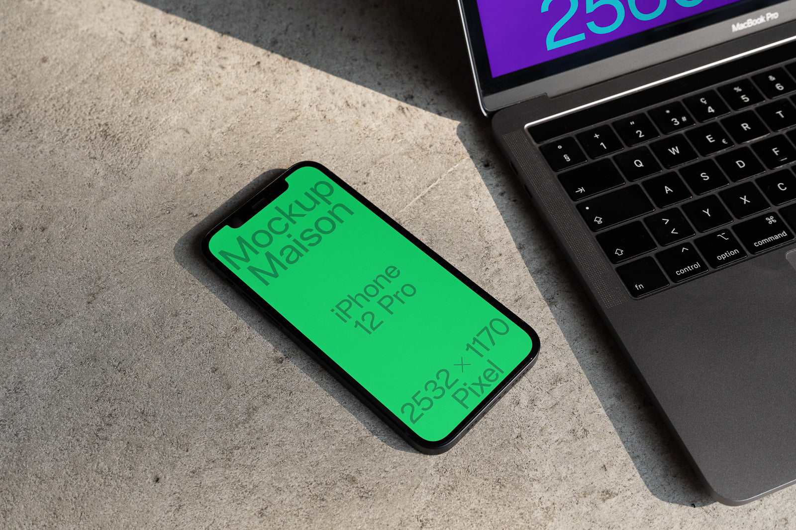 PSD mockup of an iPhone 12 Pro lying on concrete beside a laptop, displaying text "Mockup Maison" and "2532 × 1170 Pixel" on its screen.
