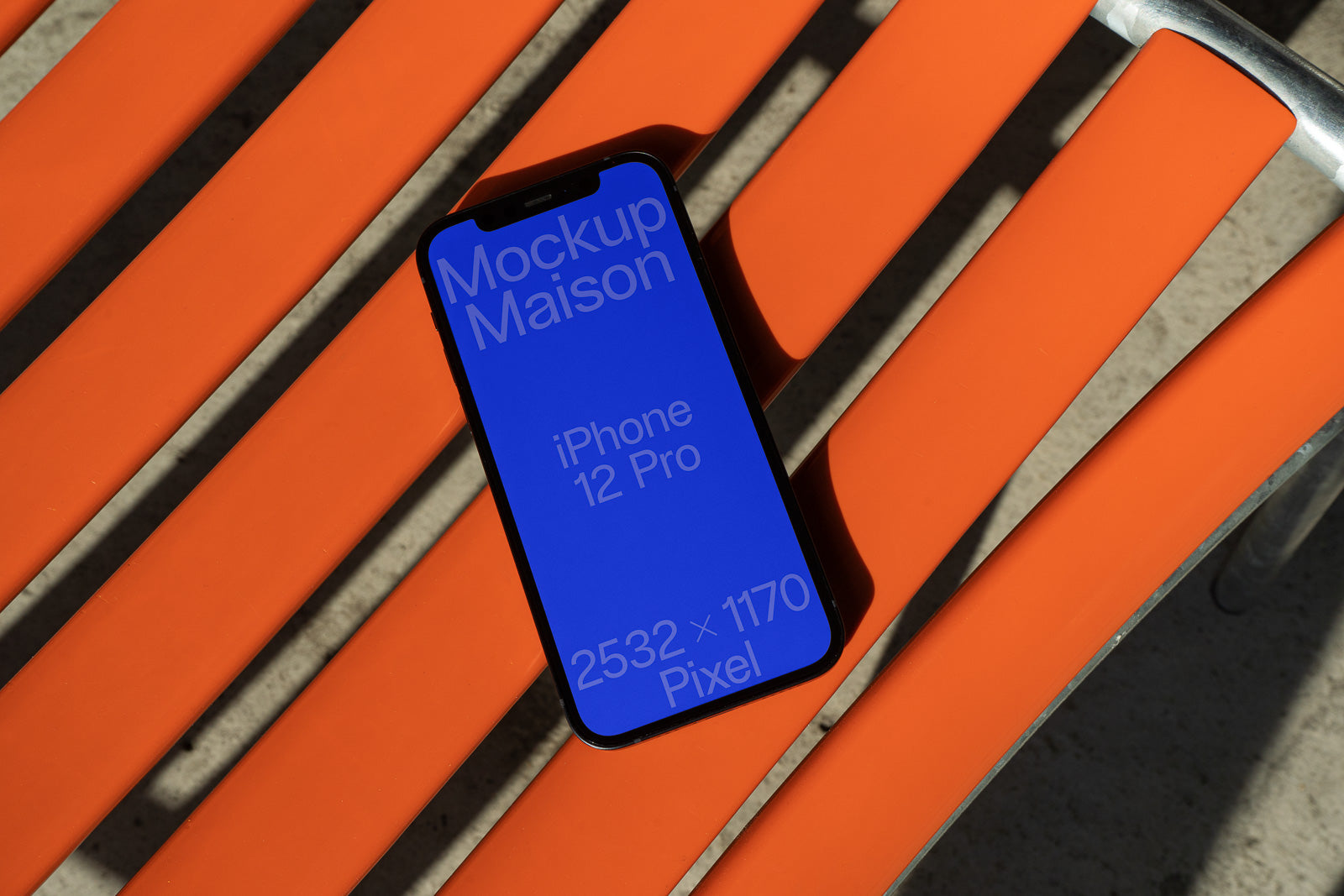 PSD mockup of an iPhone 12 Pro displaying a blue screen with text, resting on an orange slatted chair in sunlight.