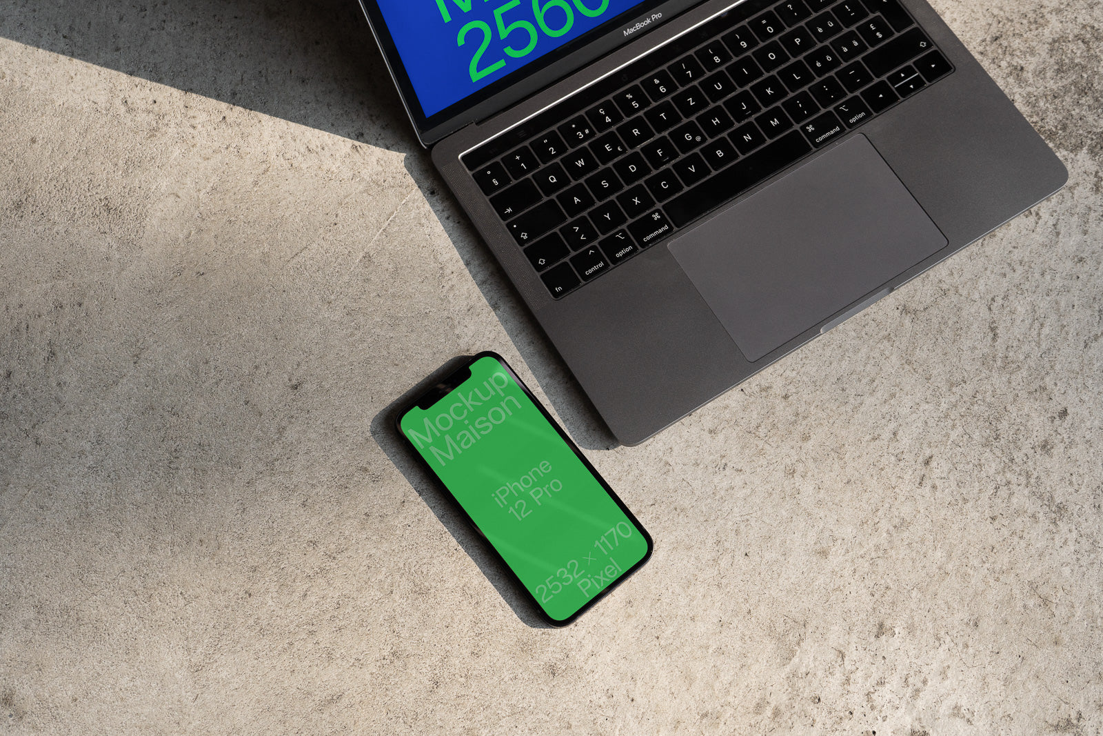 PSD mockup of a silver MacBook Pro and an iPhone 12 Pro with green screens placed on a textured concrete surface.