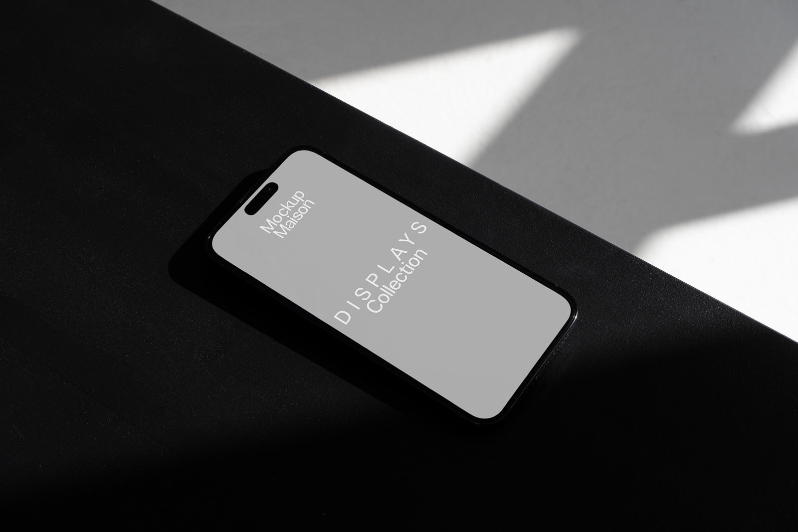 PSD mockup of a smartphone lying on a dark surface with light and shadow interplay, screen displaying "Mockup Maison, DISPLAYS Collection."