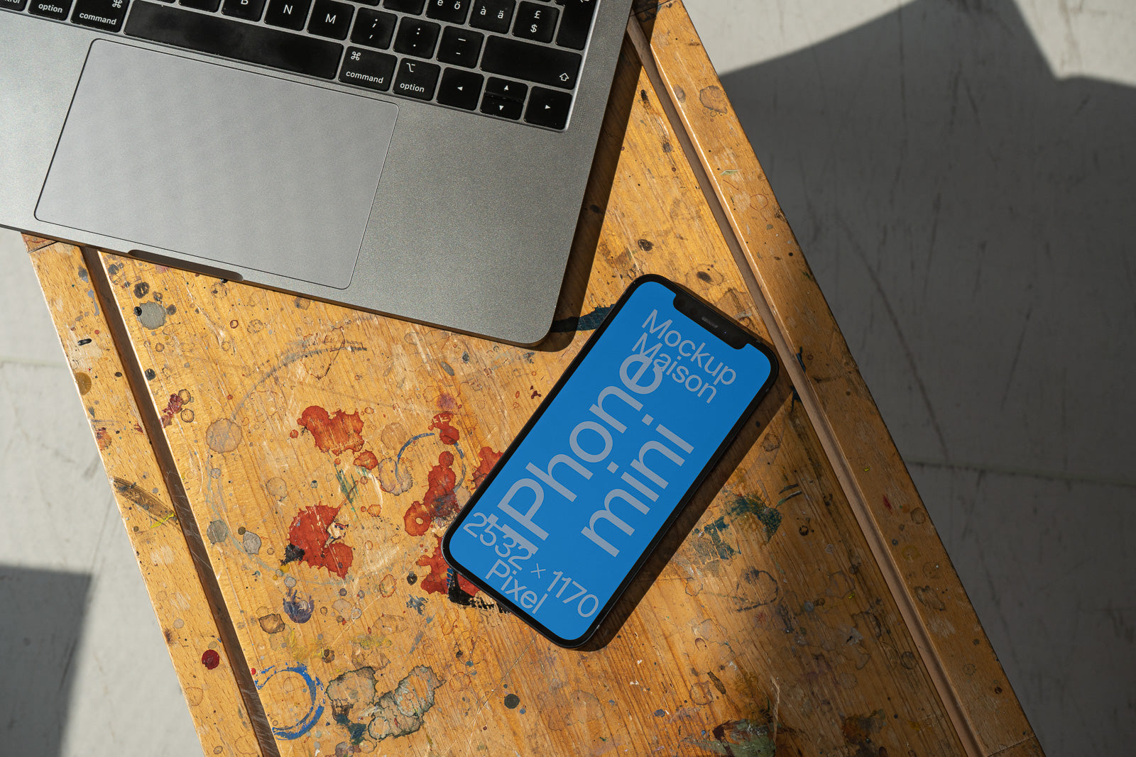 PSD mockup of a smartphone with blue screen displaying text, placed on a wooden table beside a laptop.