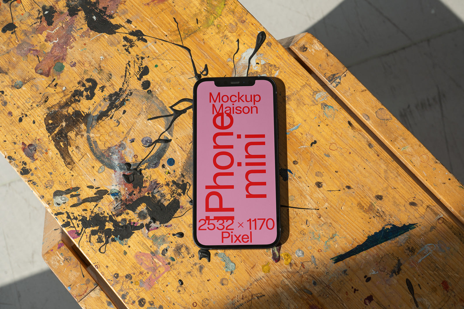 PSD mockup of a smartphone with a pink screen displaying red text, placed on a paint-splattered wooden surface, showing shadows and texture.