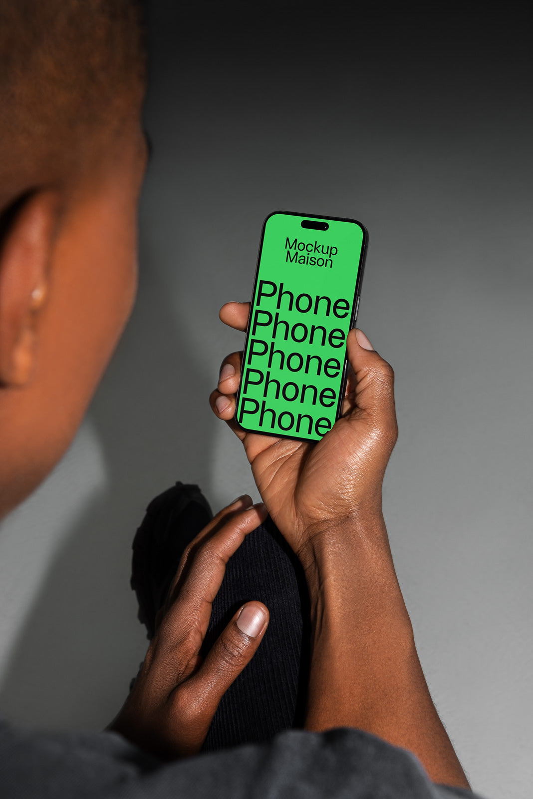 PSD mockup of a person holding a smartphone with a green screen displaying repeated text "Phone" in black, labeled "Mockup Maison".