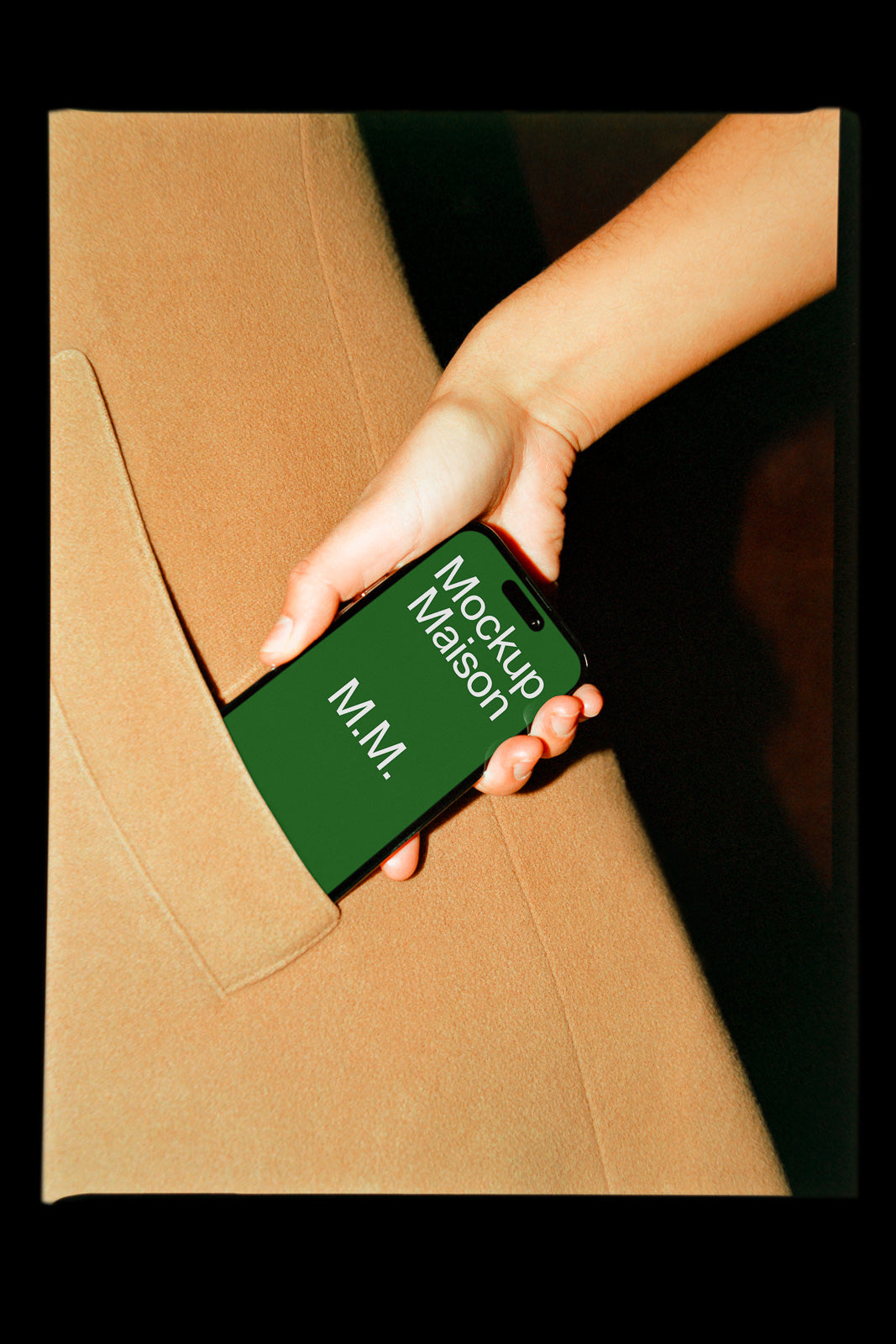 PSD mockup of a smartphone with a green screen displaying "Mockup Maison M.M." being pulled from a camel-colored coat pocket by a hand.