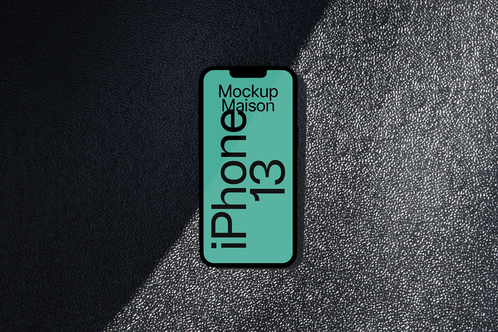 PSD mockup of iPhone 13 on textured surface with light and shadow contrast, displaying a vertical layout and green screen labeled "Mockup Maison."