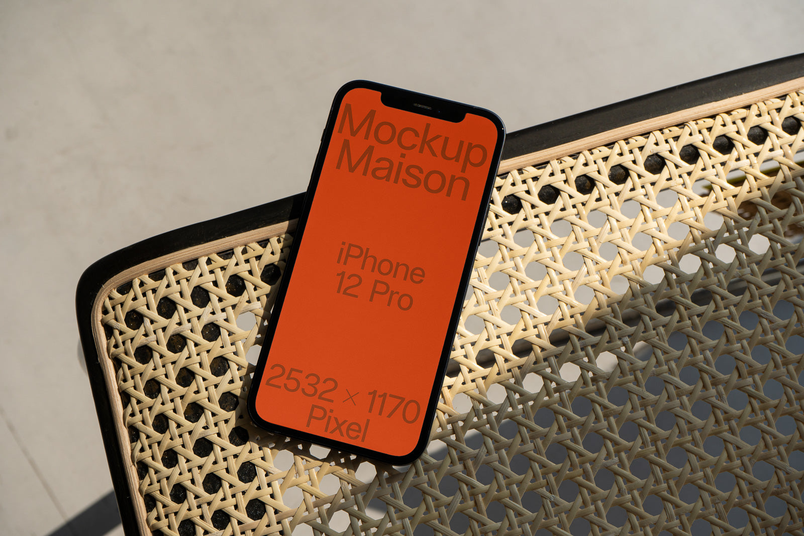 PSD mockup of an iPhone 12 Pro with an orange screen displaying text, placed on a woven rattan chair.