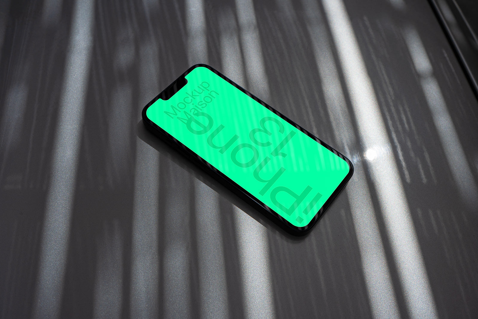 PSD mockup of a smartphone lying on a reflective surface with light patterns casting shadows, showing a green screen that reads "iPhone 13".