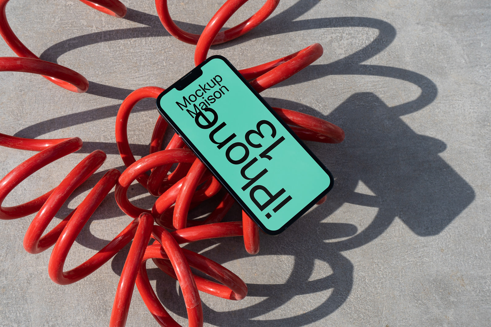 PSD mockup of a smartphone with a green screen displaying text, placed on a coiled red spring against a concrete background.