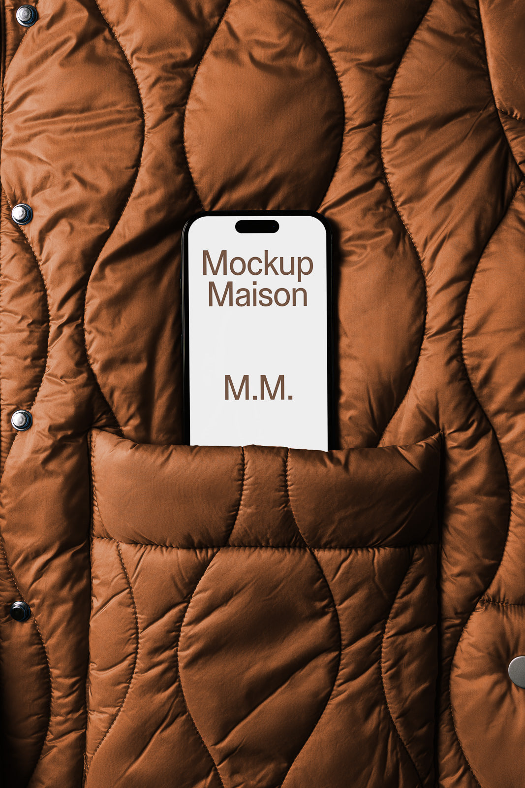 PSD mockup of a smartphone displaying "Mockup Maison M.M." text, partially tucked into a brown quilted jacket pocket with a button detail.