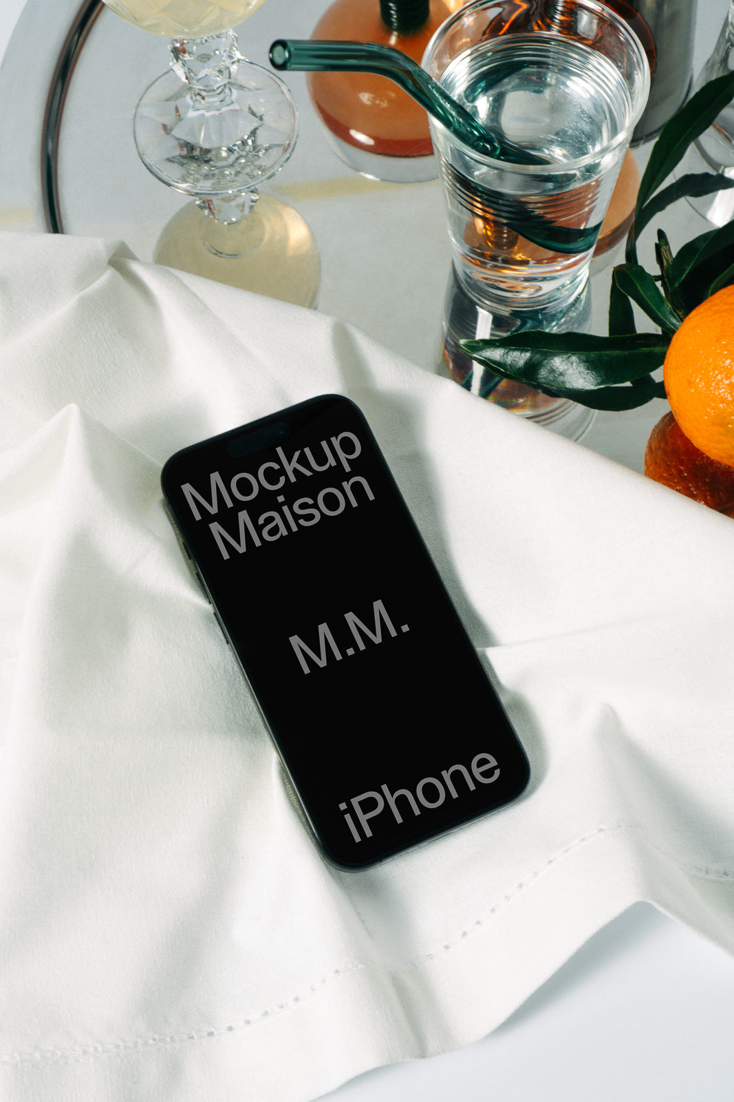 PSD mockup of a smartphone placed on a white cloth, surrounded by a glass of water and an orange, creating a modern and fresh setting.