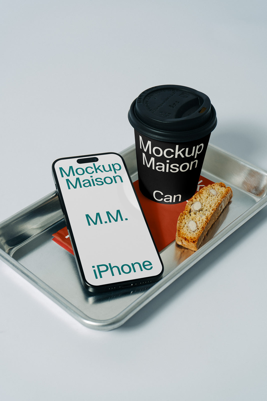 PSD mockup of a smartphone displaying "Mockup Maison" beside a black coffee cup with the same logo, placed on a metal tray with a biscotti.