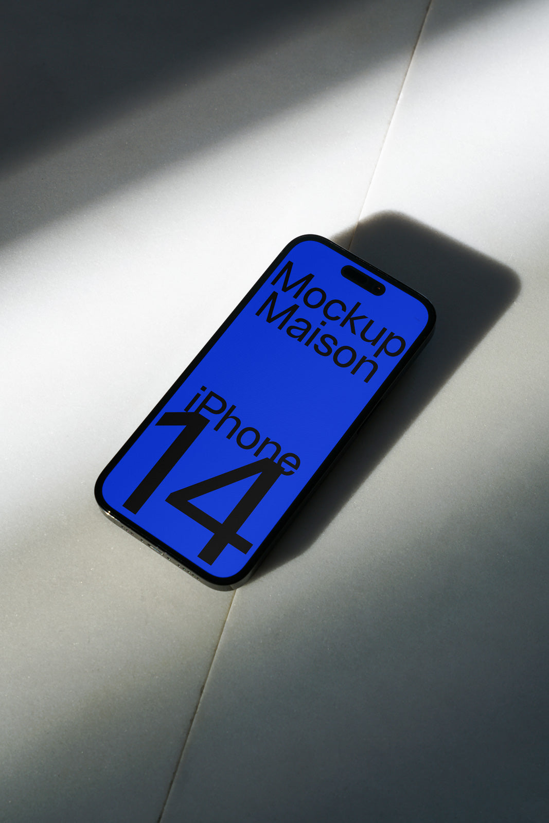PSD mockup of an iPhone 14 on a light surface with a blue display showing text "Mockup Maison."