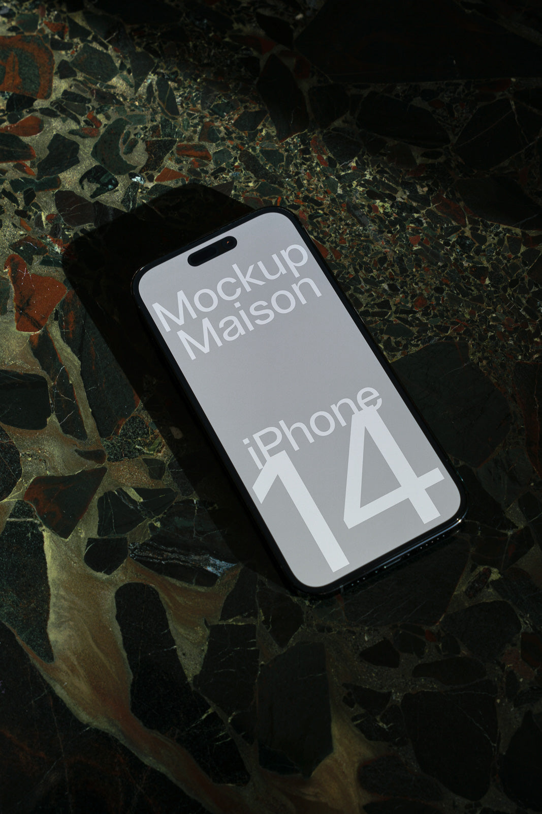 PSD mockup of iPhone 14 on a textured dark marble surface. The screen displays the words "Mockup Maison iPhone 14" in white text.