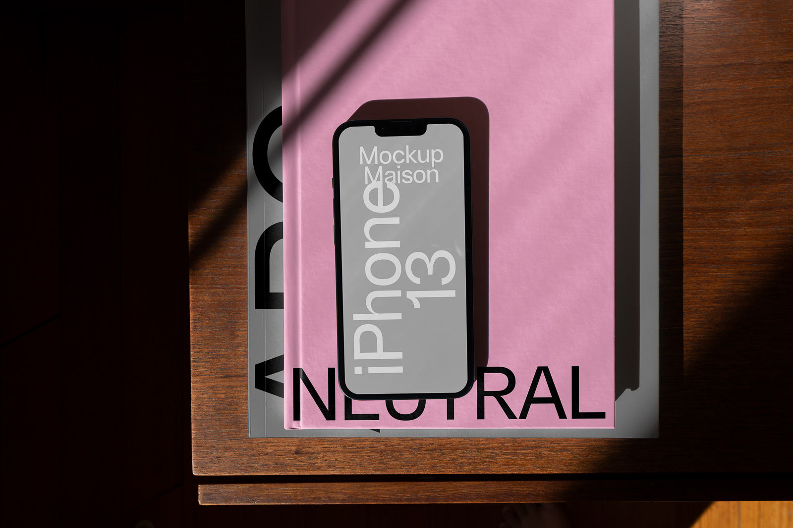 PSD mockup of an iPhone 13 placed on two books with pink and gray covers, casting a shadow on a wooden surface.
