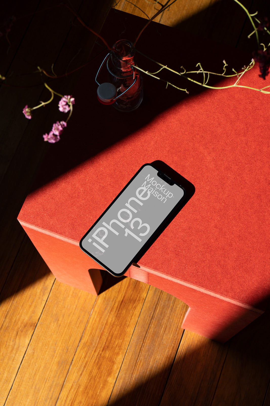 PSD mockup of an iPhone on a red table with natural sunlight and surrounding decorative elements, casting shadows on wooden floor.