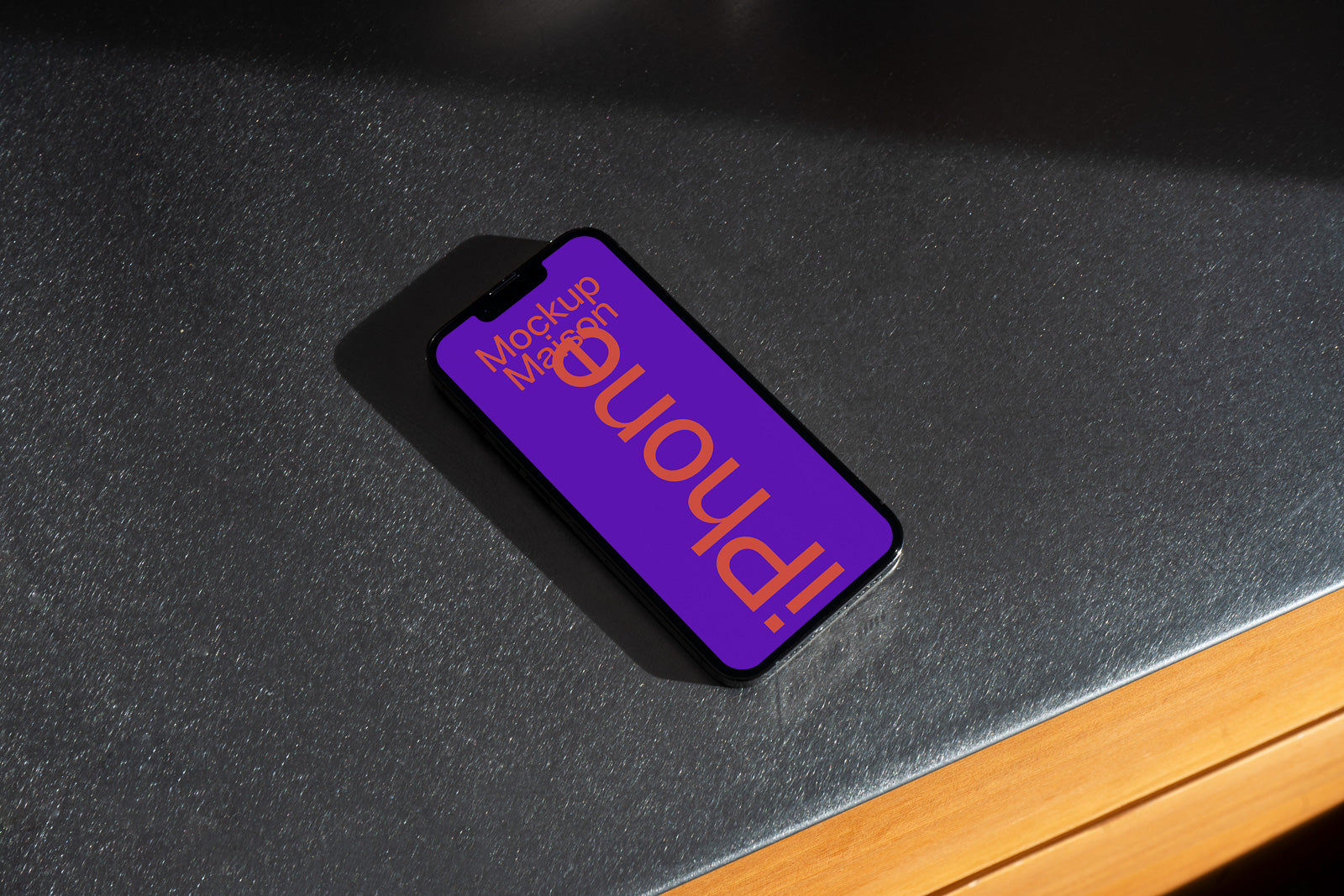 PSD mockup of a black smartphone lying on a textured dark surface with screen displaying colorful stylized text in purple and orange design.