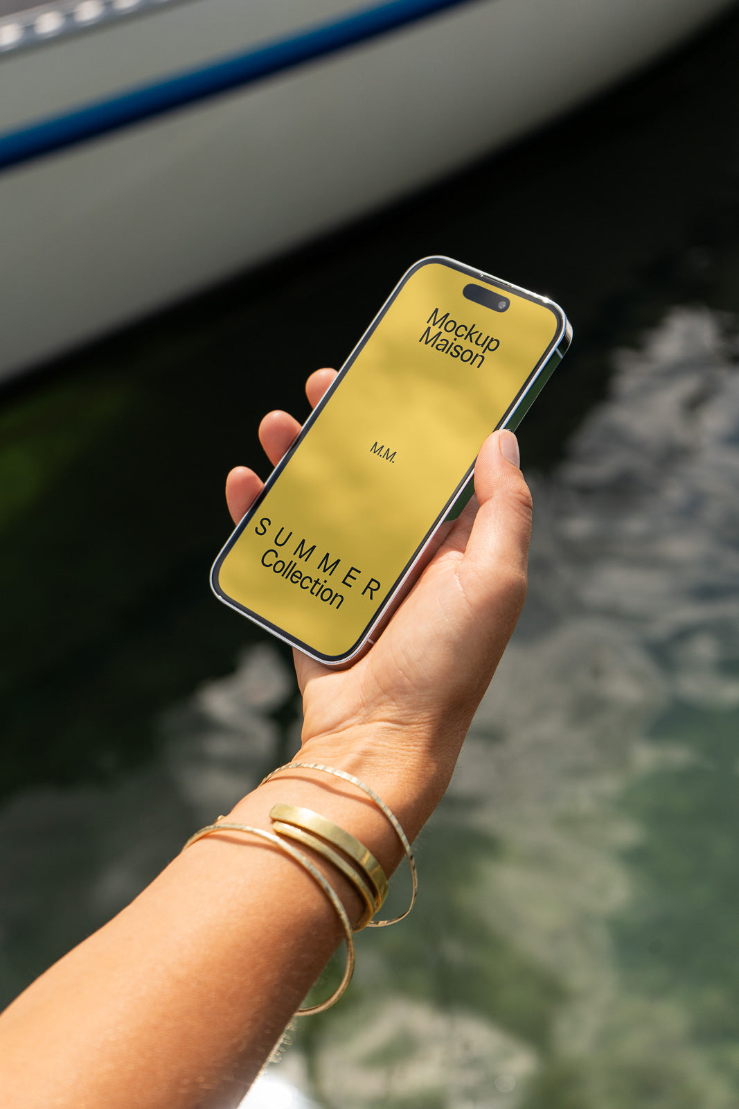 PSD mockup of a hand holding a smartphone displaying "Mockup Maison" and "Summer Collection," set against a blurred outdoor background.