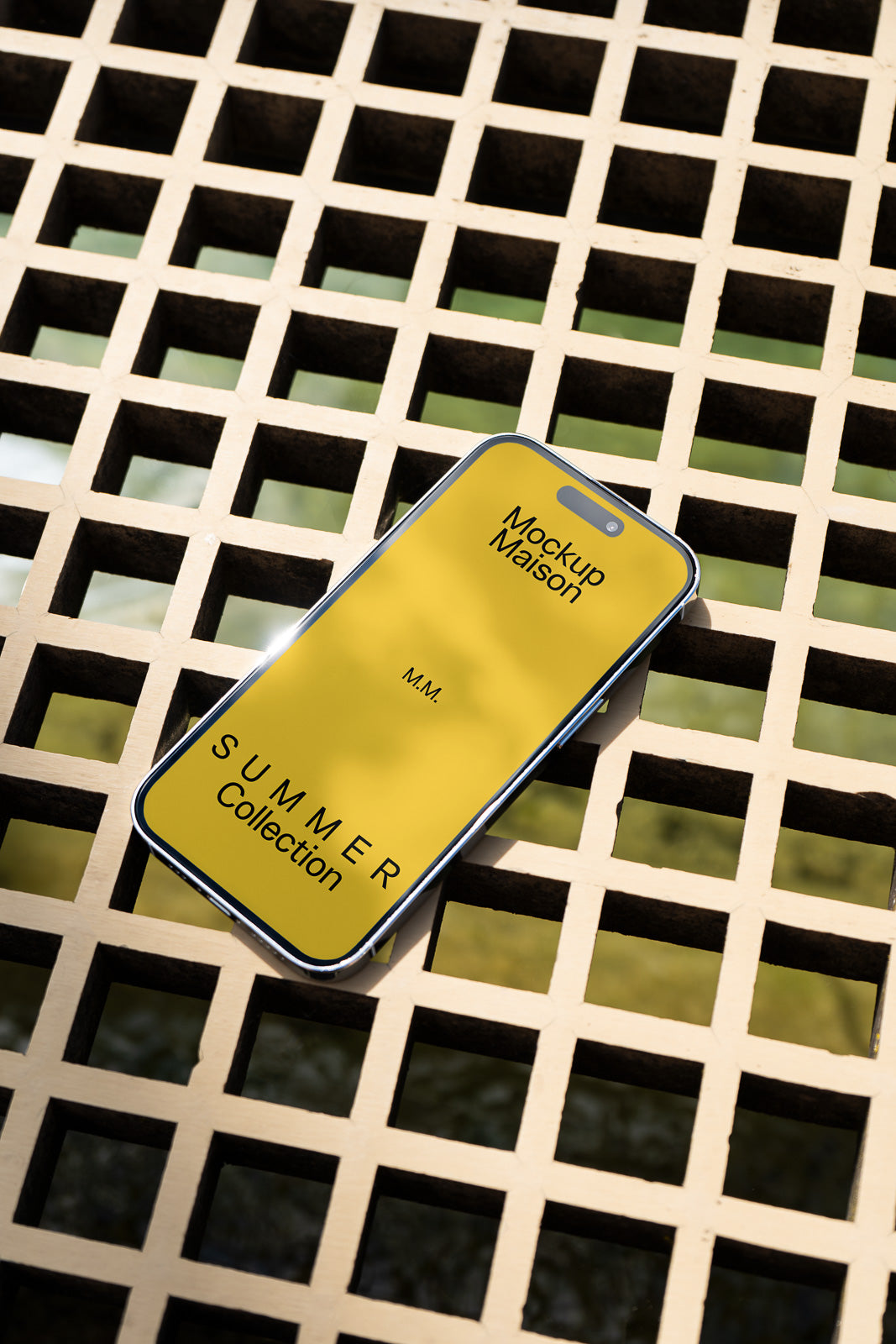 PSD mockup of a smartphone displaying a yellow screen with "Mockup Maison" and "SUMMER Collection" text, placed on a lattice surface.