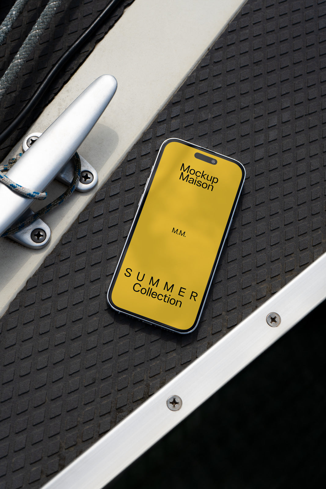PSD mockup of a smartphone displaying a yellow screen with "Mockup Maison" text, placed on a textured surface near a metal boat cleat.