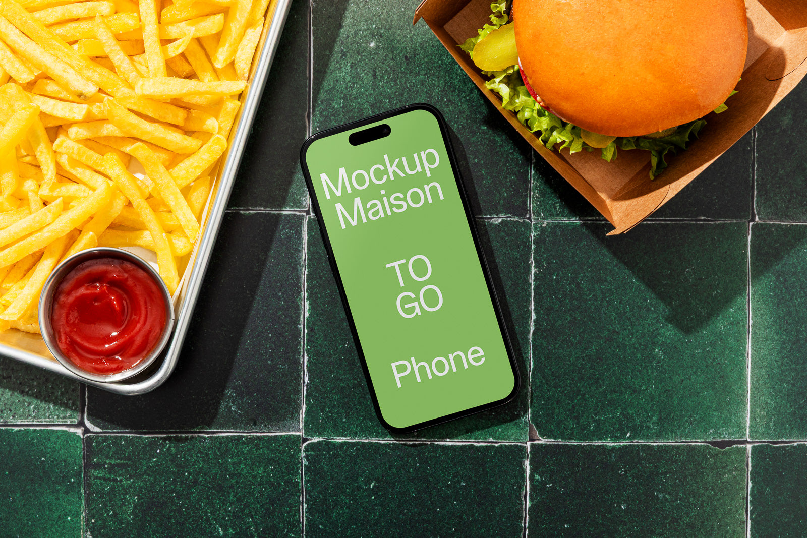 PSD mockup of a smartphone on a green tiled surface between a tray of fries with ketchup and a takeout burger in a carton box.