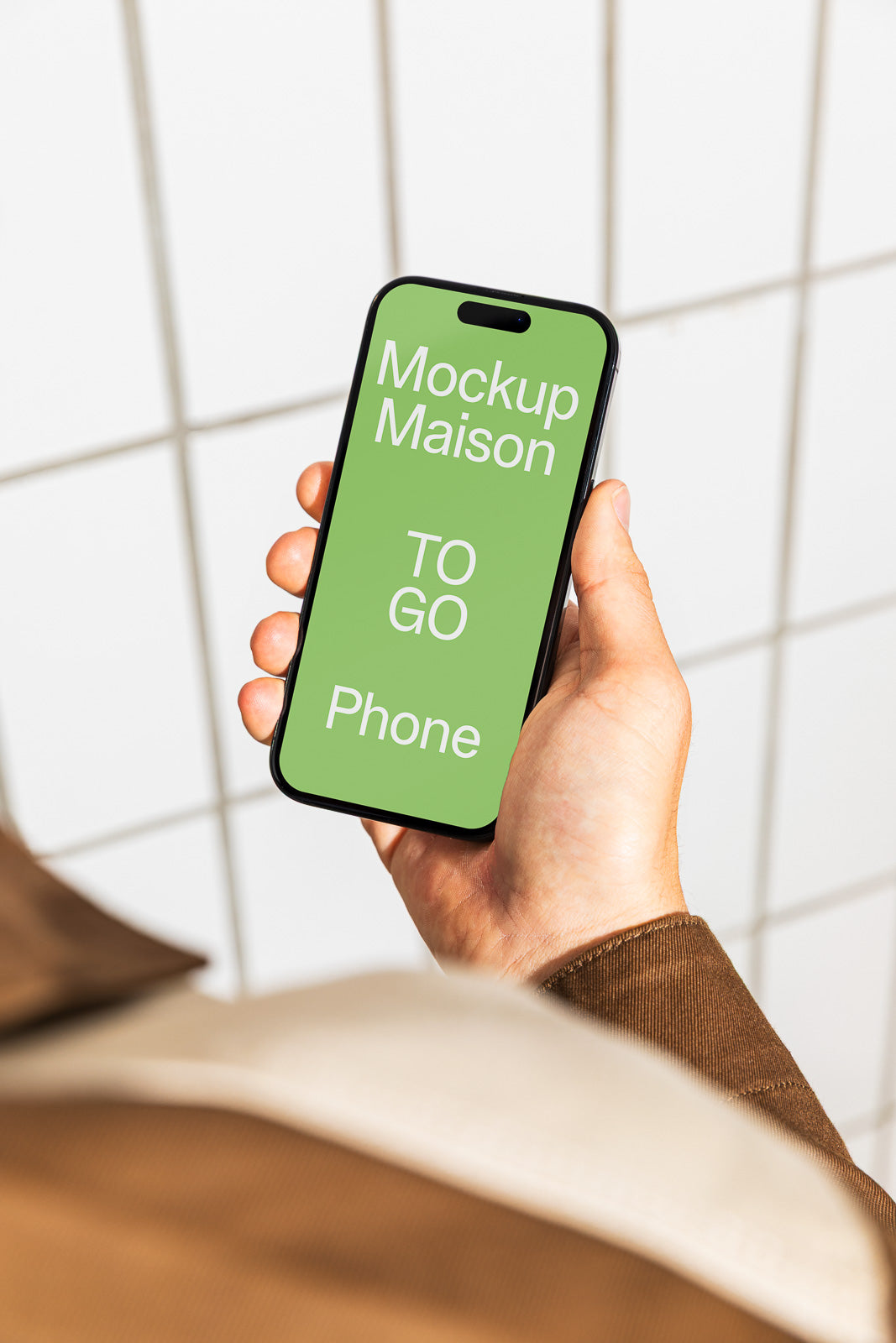 PSD mockup of a person holding a smartphone displaying "Mockup Maison TO GO Phone" on a green screen, set against a tiled background.