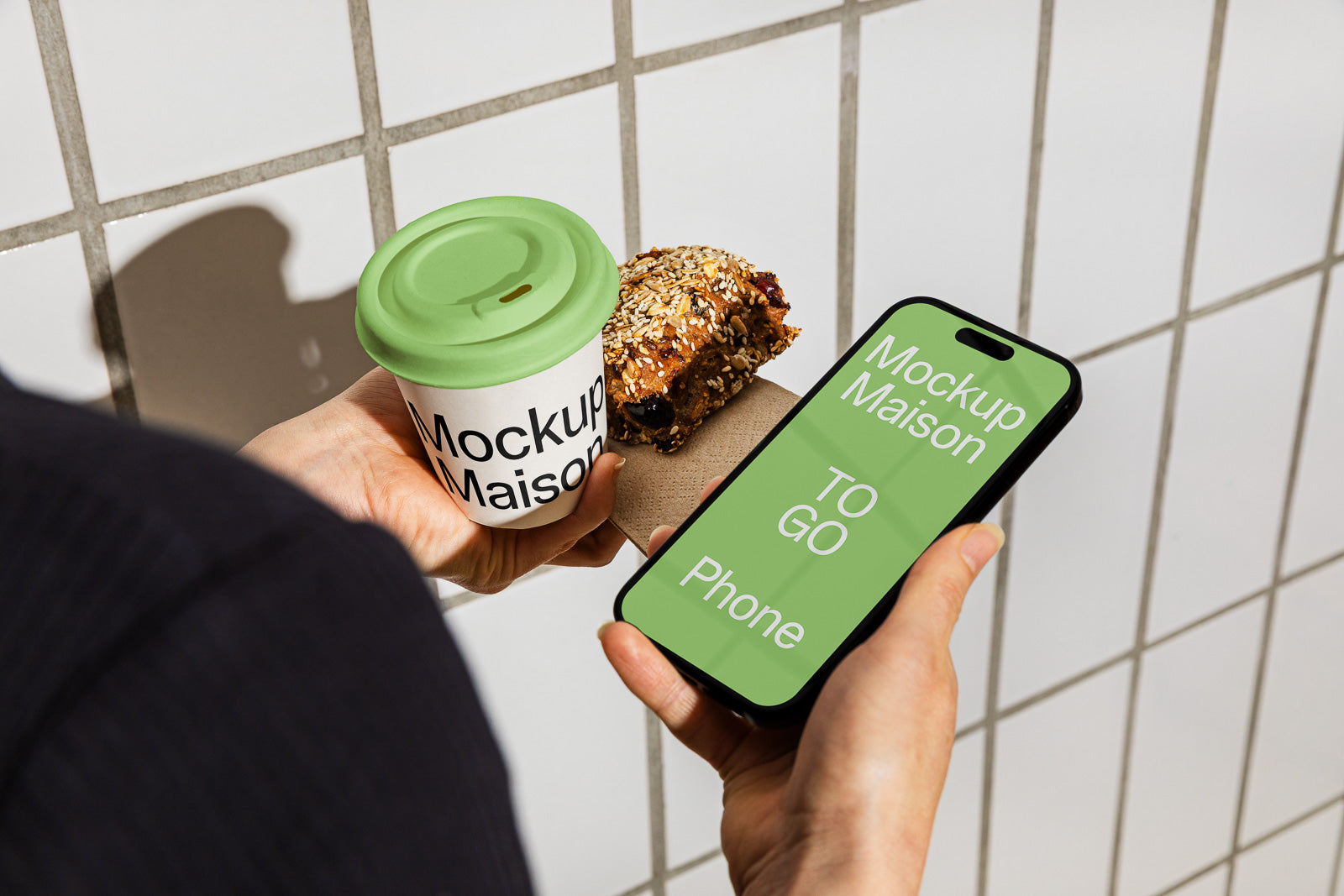 PSD mockup of a takeaway coffee cup with green lid, smartphone displaying text, and a seeded pastry, all held against a tiled background.