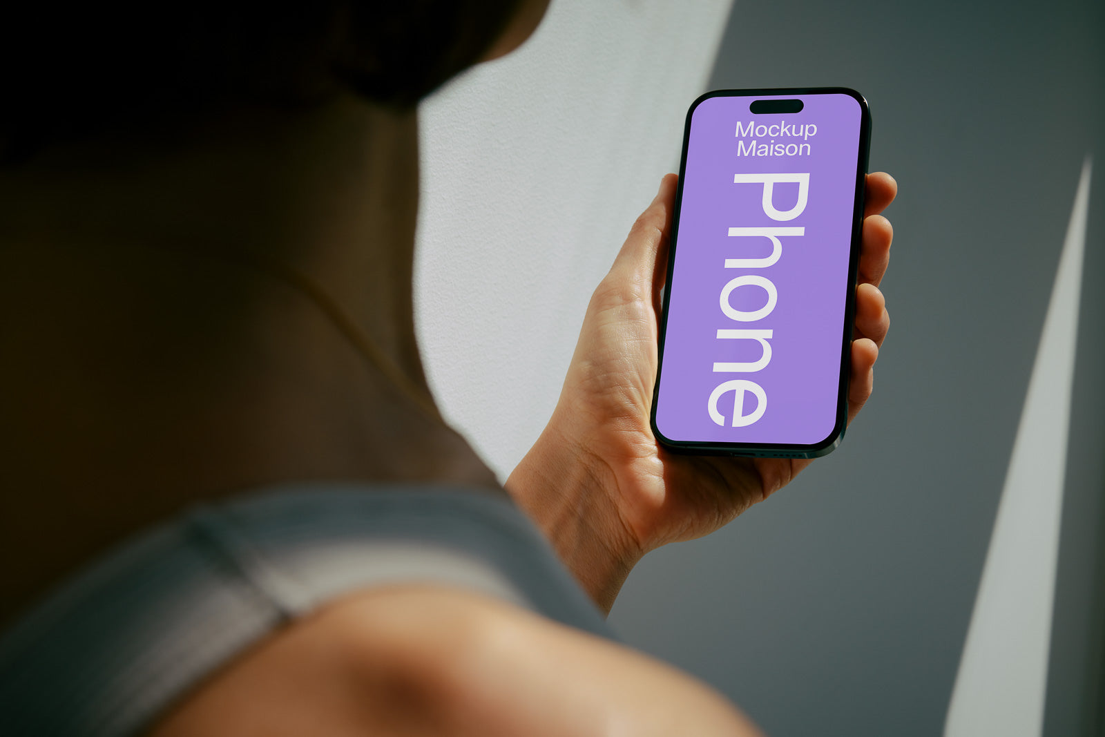 PSD mockup of a smartphone held in a person's hand, displaying a purple screen with text that reads “Mockup Maison Phone.” The background is softly lit.