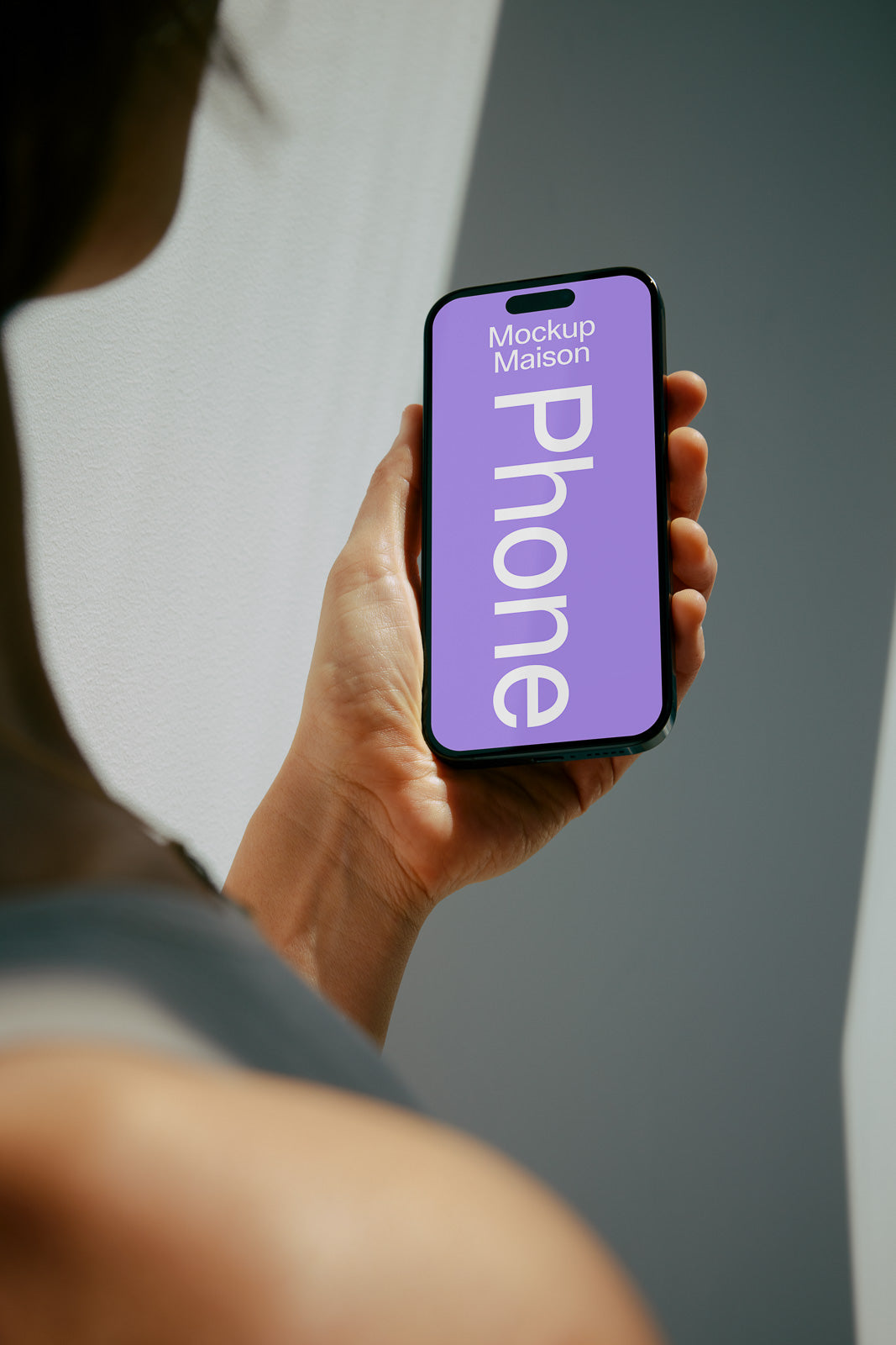 PSD mockup of a hand holding a smartphone with a purple screen displaying the text "Mockup Maison Phone" against a softly lit background.