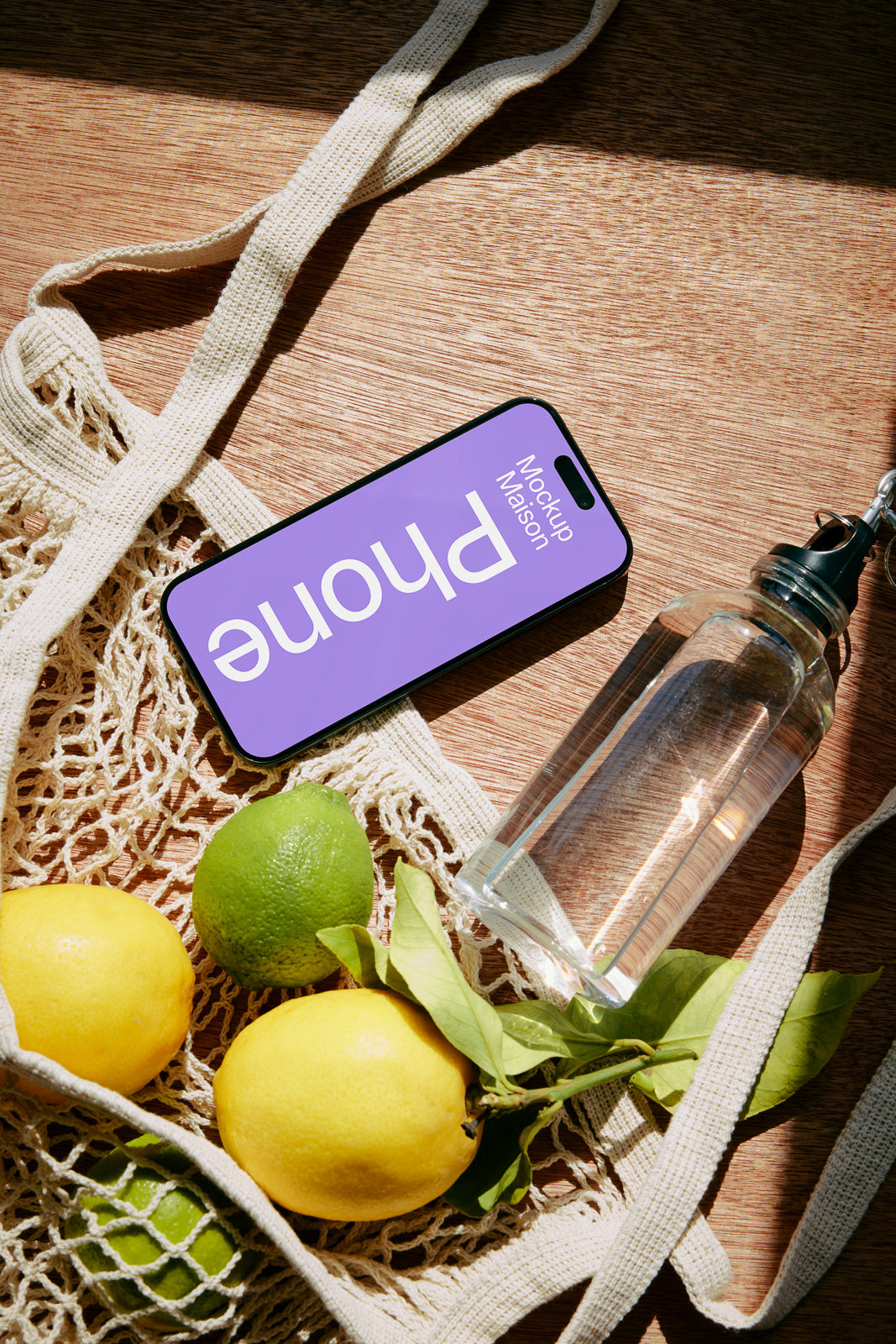 PSD mockup of a smartphone lying on a table with a netted bag, lemons, limes, and a water bottle.