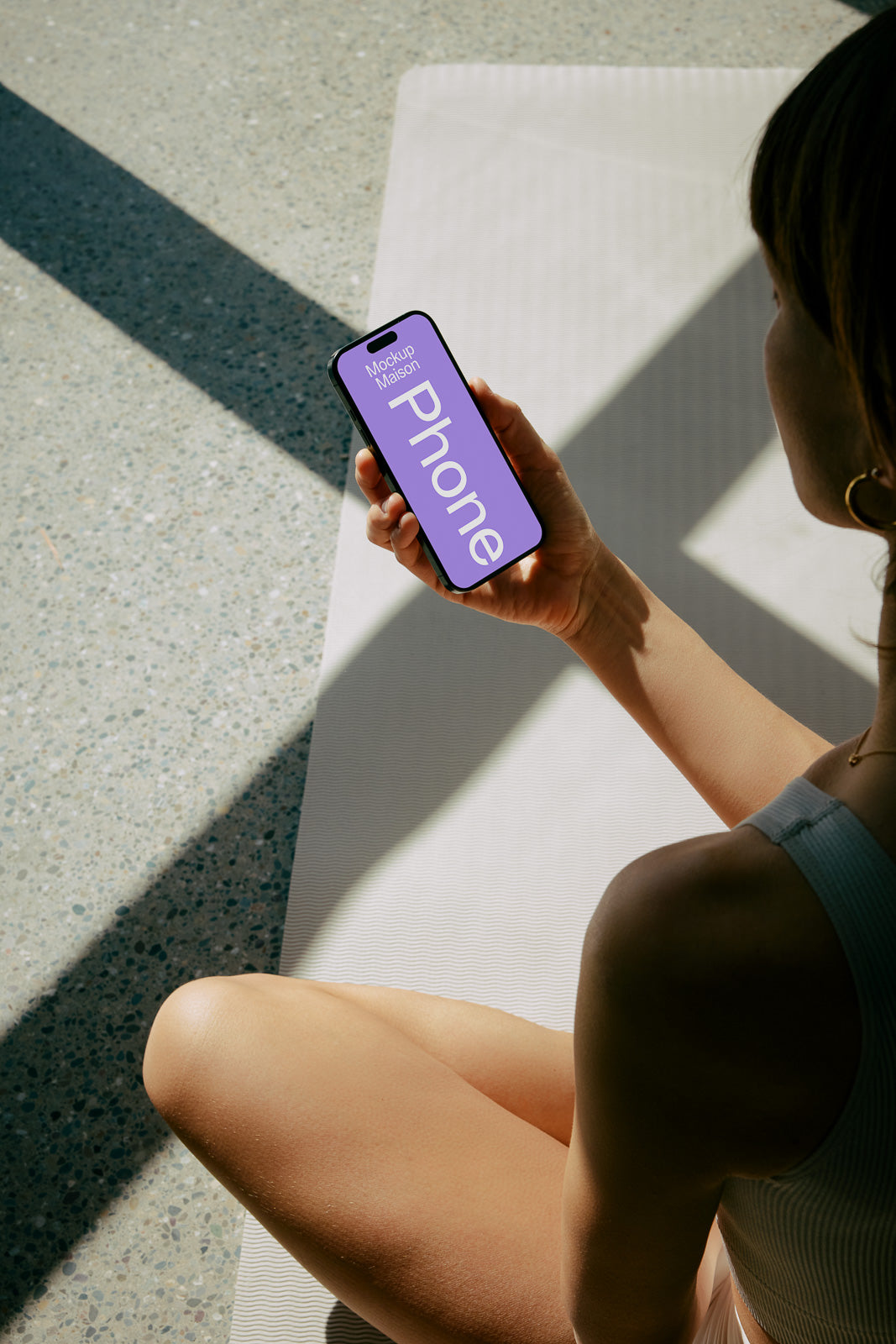 PSD mockup of a smartphone held by a person seated on a yoga mat, screen displaying "Phone" with sunlight casting shadows.