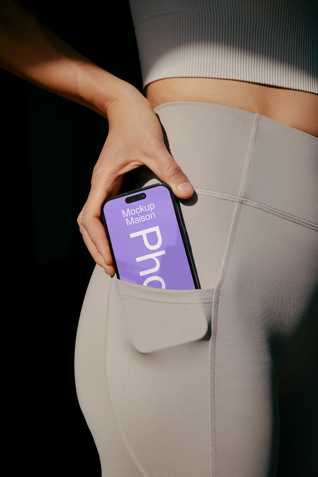 PSD mockup of a smartphone with a purple screen partially tucked into the pocket of light gray leggings worn by a person in a ribbed top.