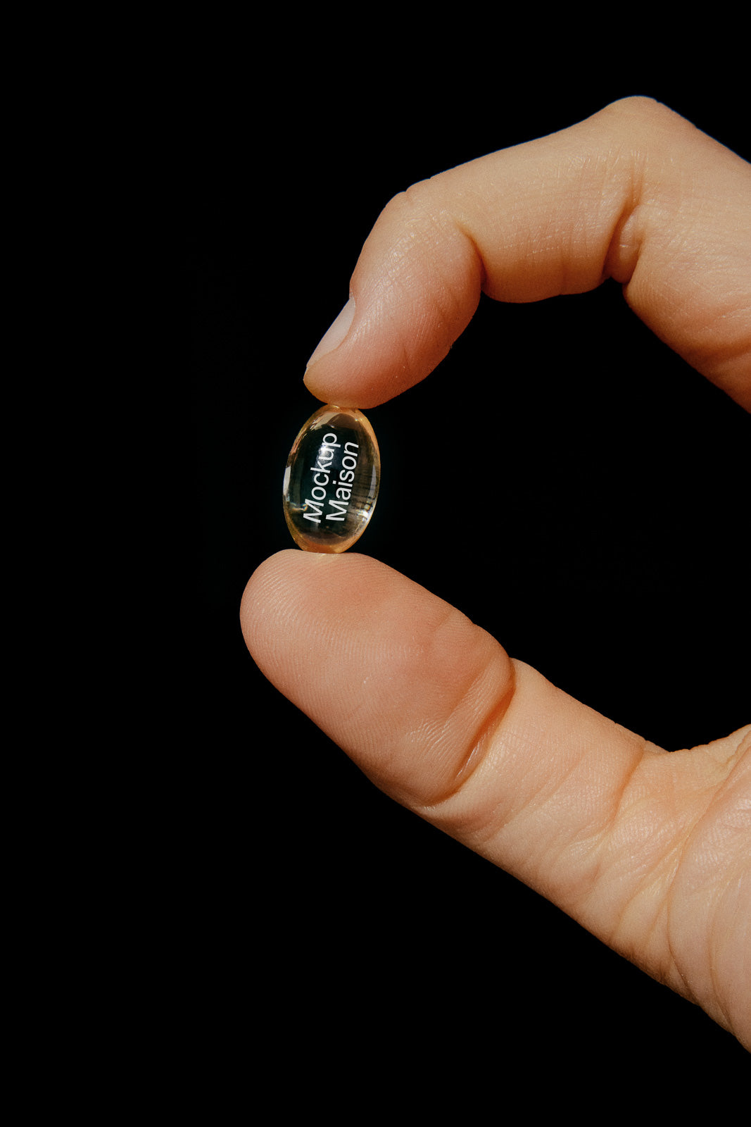 PSD mockup of a person's hand holding a transparent capsule with text "Mockup Maison" visible, set against a black background.