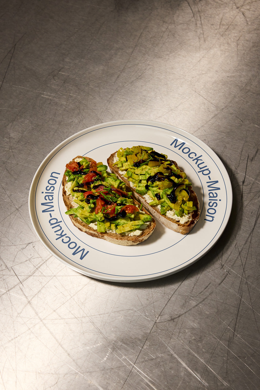 PSD mockup of two avocado toast slices with toppings on a white plate decorated with the text "Mockup Maison" placed on a metal surface.
