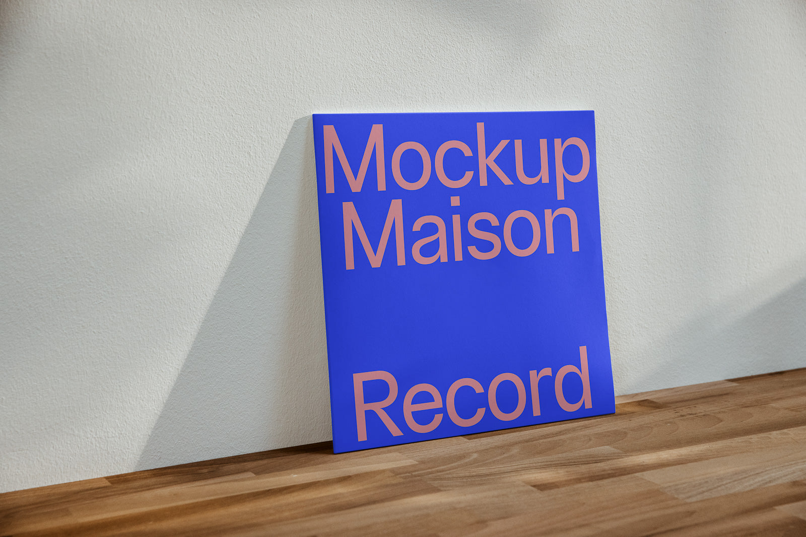 PSD mockup of a square blue record cover with large pink text leaning against a white wall on a wooden surface.