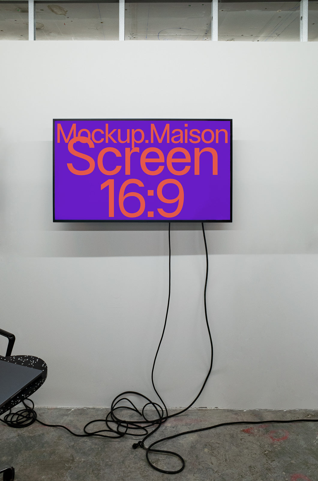 PSD mockup of a 16:9 screen mounted on a wall displaying bold text "Mockup.Maison" with visible cables hanging below.